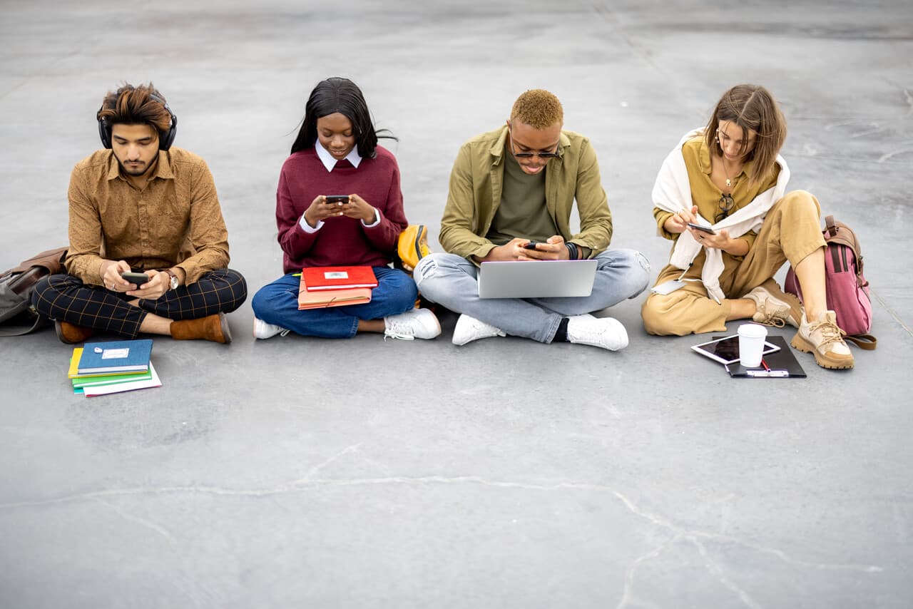 a group of students sitting on asphalt and dealing with their digital devices