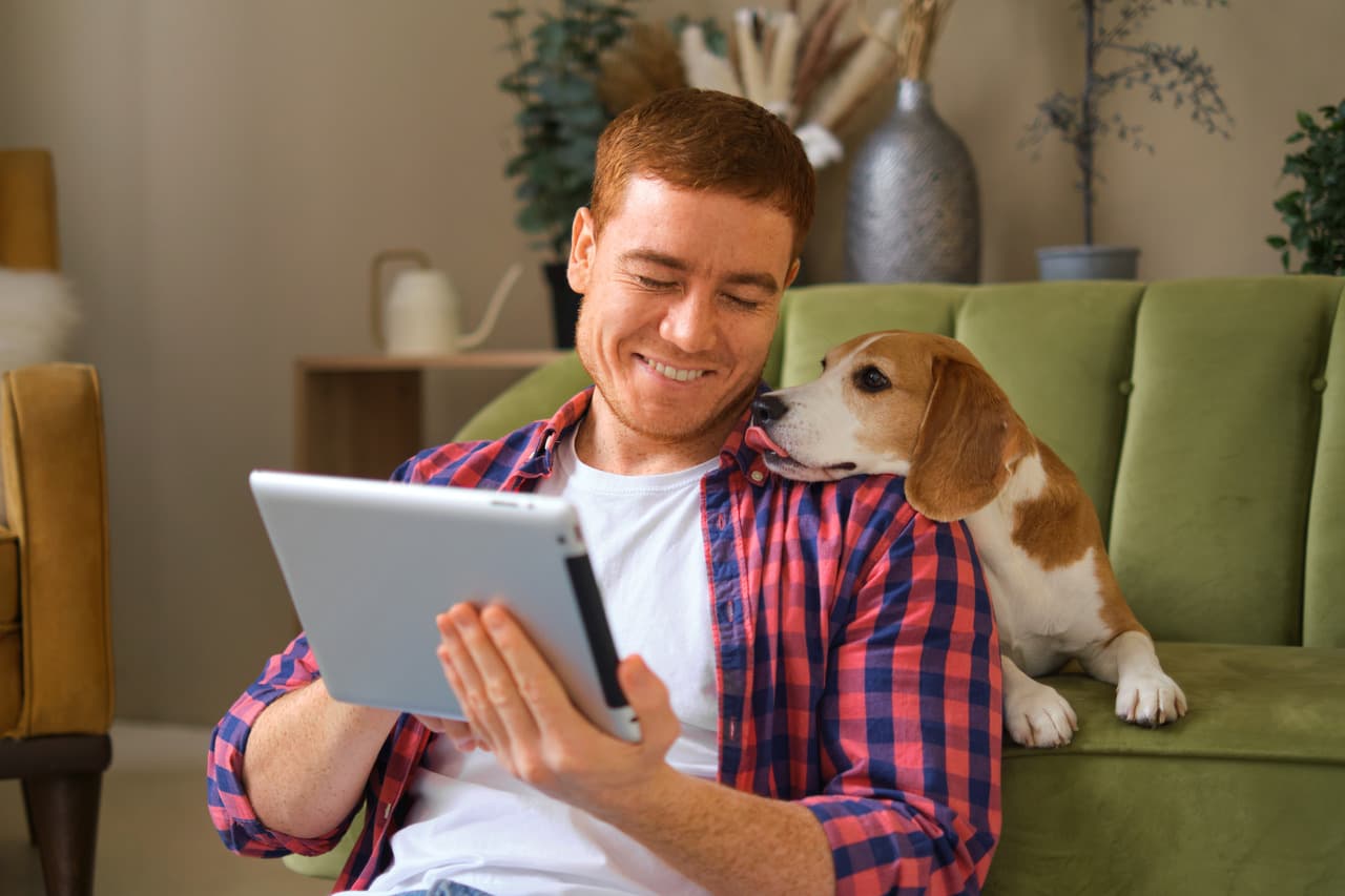 a man sitting and navigating his tablet with his dog at home
