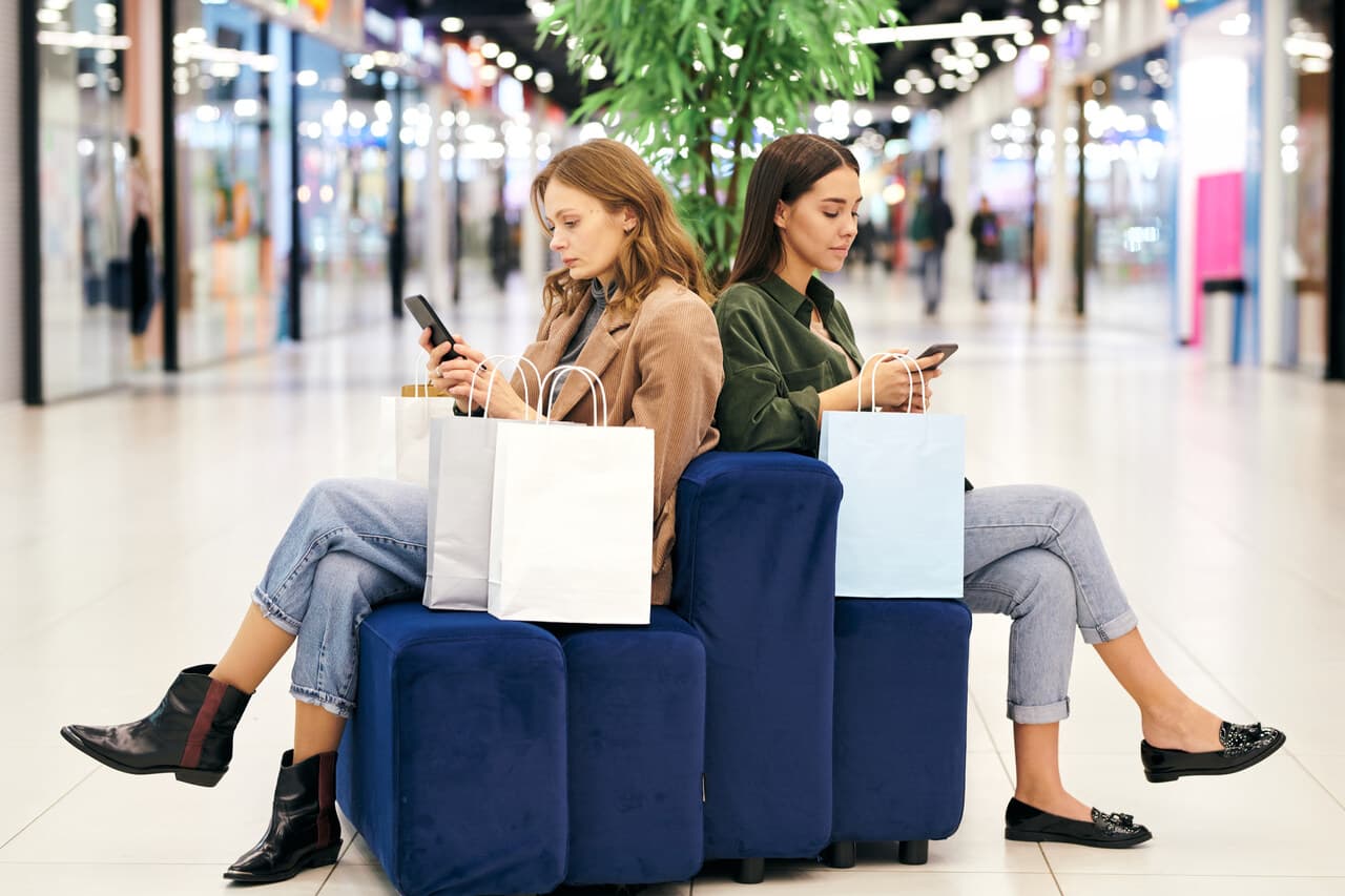 women sitting in a shopping mall and searching for special offers