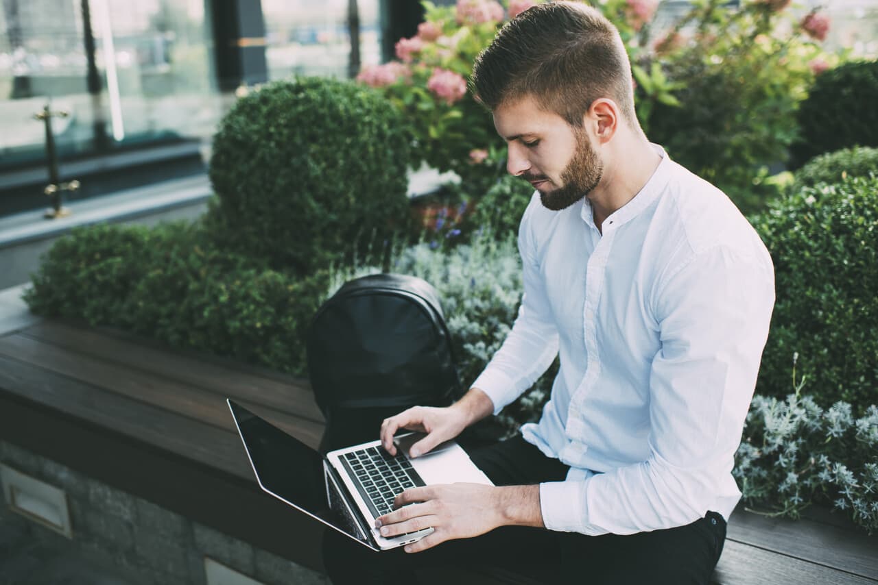 a man checking his laptop seriously and sitting on a street