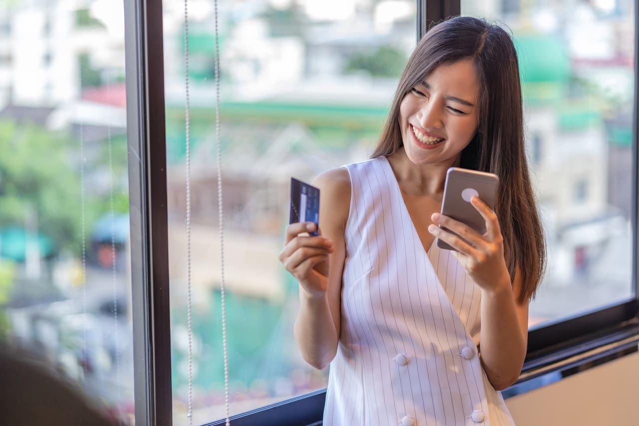 a woman smiling and being happy with the shopping she has by holding a credit card and a mobile phone in her hands