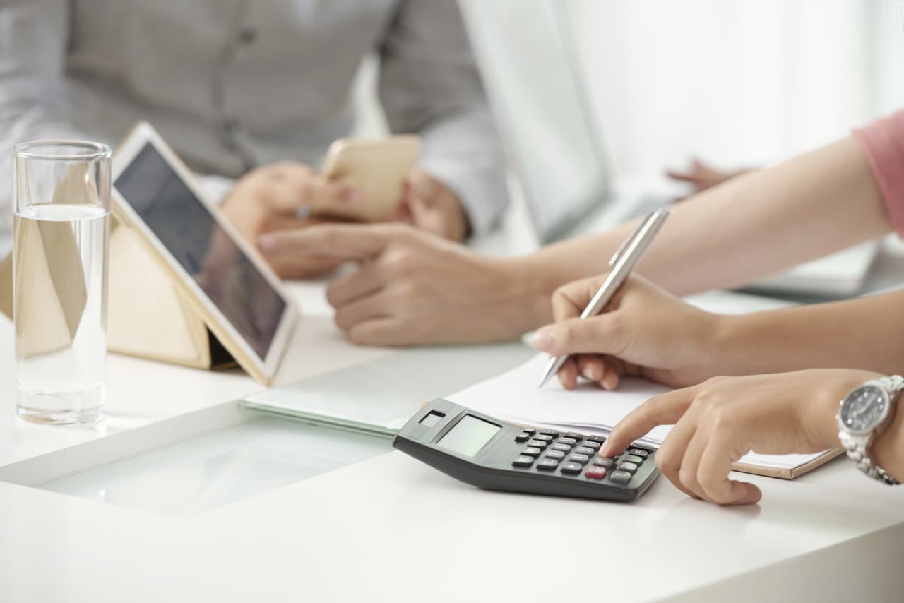 a cropped photo of a woman using calculator and writing the results