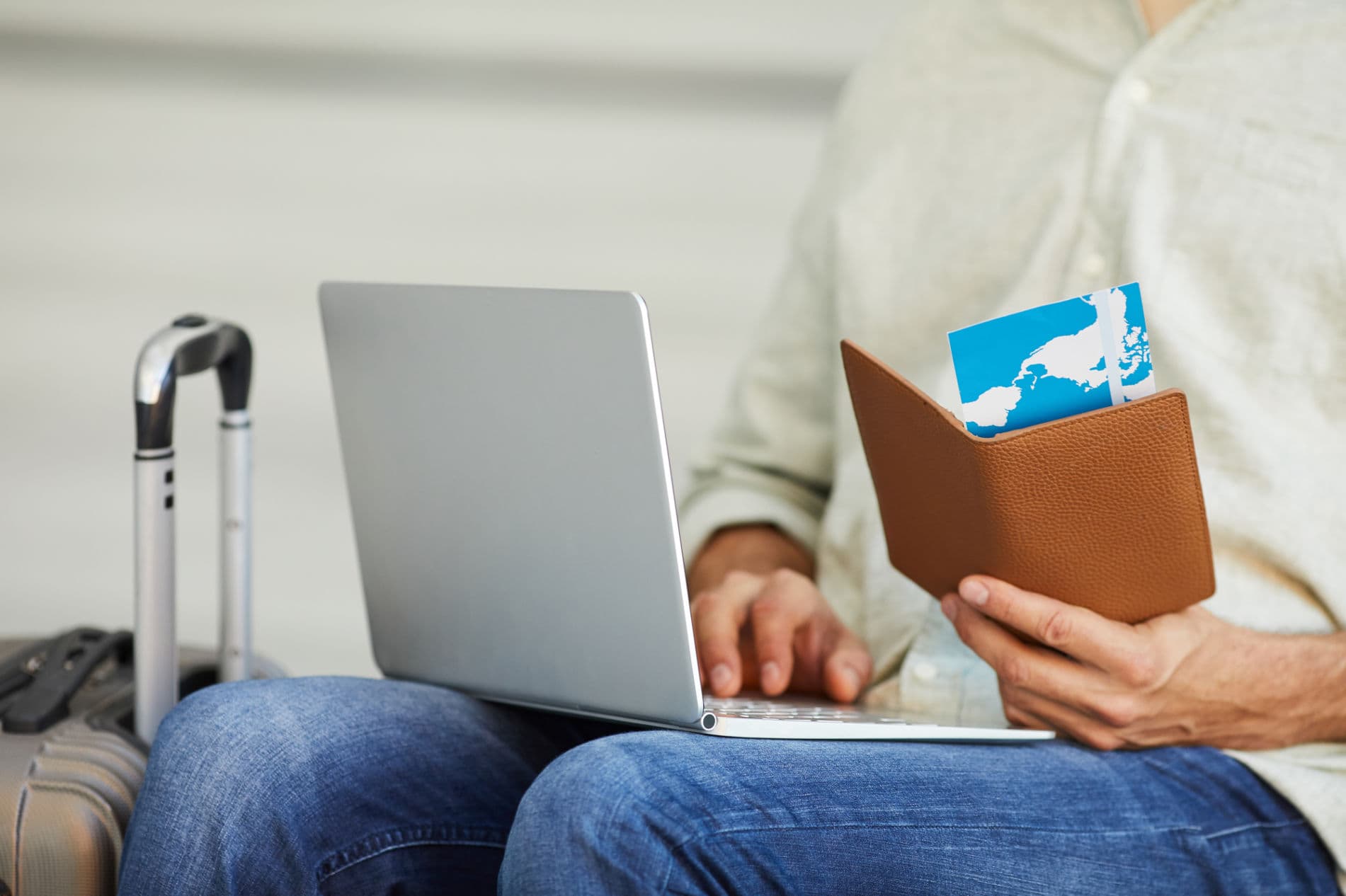 A man sitting on a chair with a laptop and a ticket, ready for travel