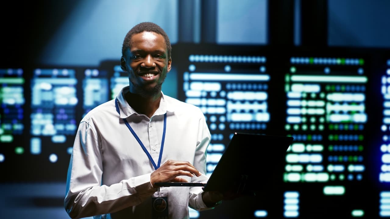 a man standing and smiling to the camera, a computer in his hand