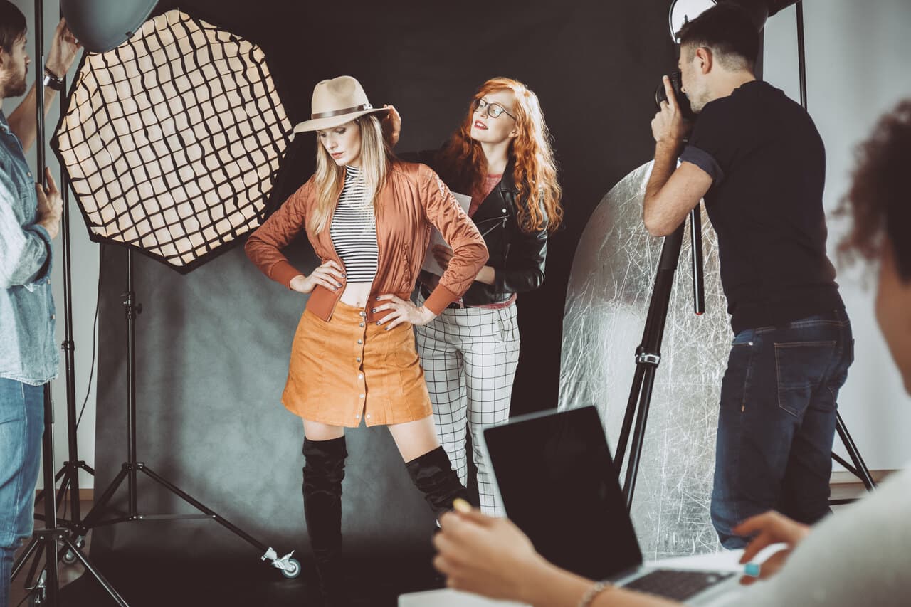 stylist and professional model among a group of people in a studio with a camera